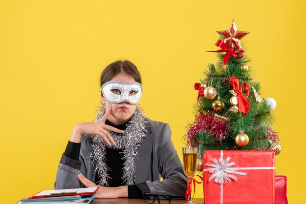 Vue avant de penser fille avec masque assis à la table en mettant le doigt