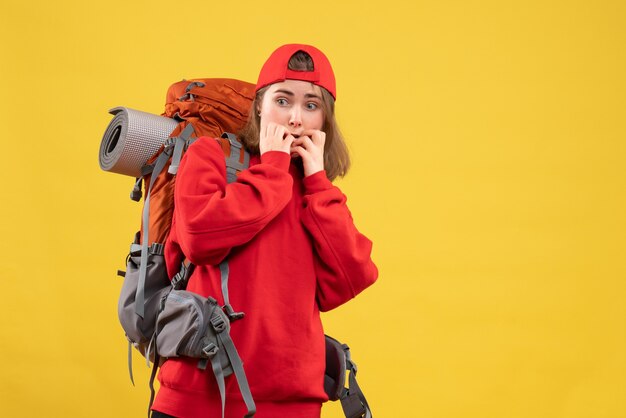 Vue avant perplexe voyageur féminin avec sac à dos debout sur le mur jaune