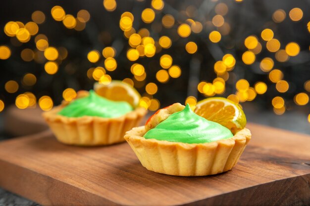 Vue avant de petites tartes sur une planche à découper sur les lumières de Noël surface sombre