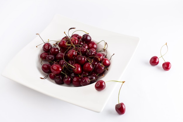 Vue avant de la plaque avec des cerises aigres et moelleuses sur blanc