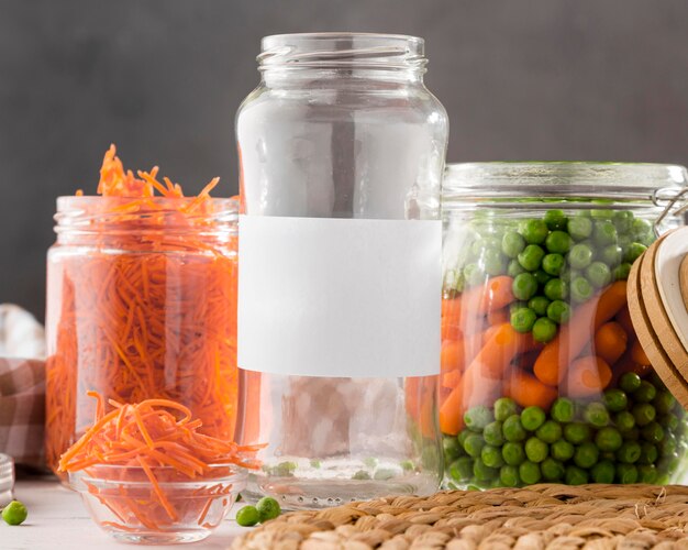 Vue avant des pois marinés et des carottes miniatures dans des bocaux en verre transparent