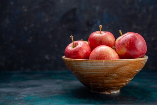 Vue avant des pommes rouges fraîches juteuses et moelleuses à l'intérieur de la plaque sur le bureau bleu foncé fruits frais doux vitamine vitamine