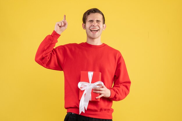 Vue avant ravi jeune homme aux yeux fermés tenant cadeau sur jaune