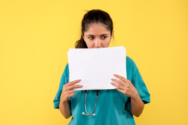 Vue avant réfléchie femme médecin avec des documents debout sur fond jaune