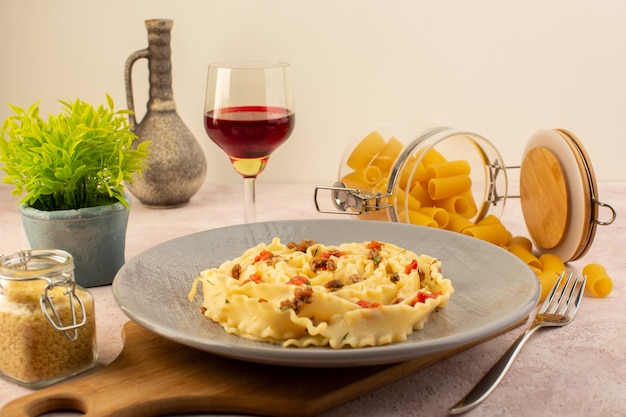 Photo gratuite une vue avant repas savoureux de pâtes italiennes avec des légumes cuits et de petites tranches de viande à l'intérieur de la plaque grise avec des fleurs et des pâtes crues sur rose