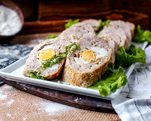 Vue avant roule délicieux pâté délicieux avec salade verte à l'intérieur de la plaque blanche sur la surface brune