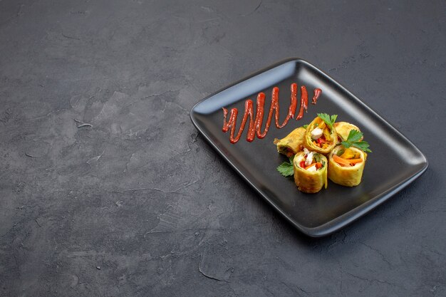 Vue avant des rouleaux de pâté de légumes à l'intérieur de la plaque noire sur une surface sombre