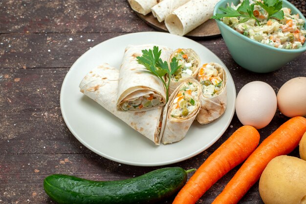 Vue avant des rouleaux de sandwich lavash en tranches avec de la salade et de la viande à l'intérieur avec de la salade avec des légumes sur bois