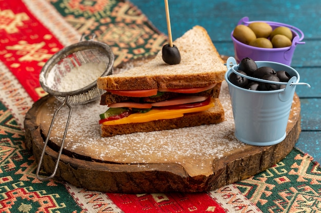 Vue avant de savoureux sandwich au pain grillé avec du jambon au fromage à l'intérieur avec des paniers de farine aux olives sur bleu