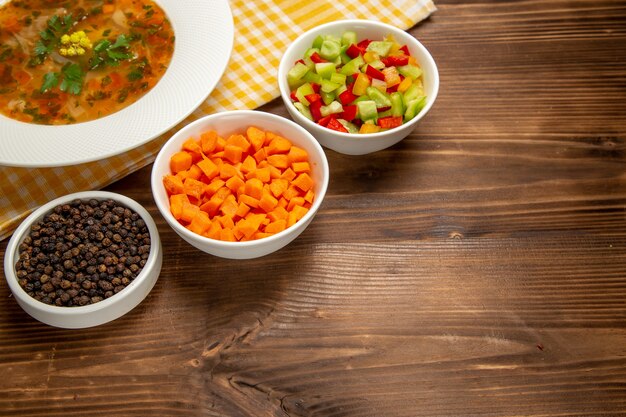 Vue avant de la soupe aux légumes savoureuse avec des légumes tranchés sur un bureau en bois brun
