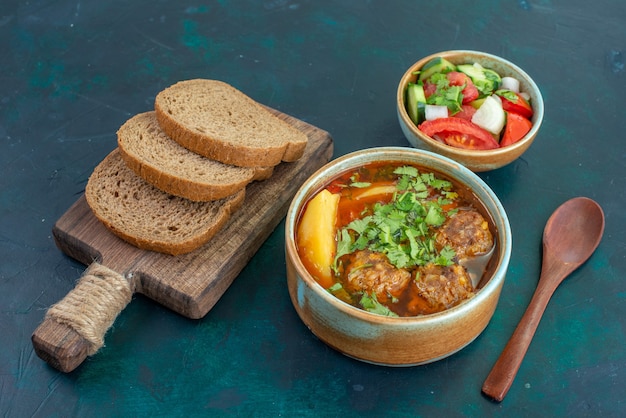 Vue avant de la soupe à la viande avec des boulettes de viande verts et des pommes de terre en tranches avec des miches de pain sur un plat de légumes sauce soupe alimentaire bureau bleu foncé