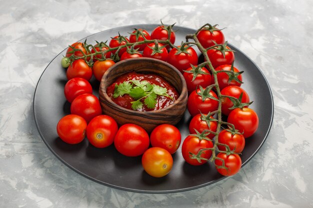 Vue avant des tomates cerises fraîches à l'intérieur de la plaque avec sauce tomate sur la surface blanche salade de légumes repas nourriture santé