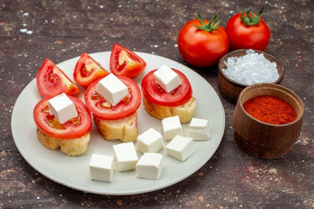 Vue avant des tomates et du fromage à l'intérieur de la plaque blanche avec assaisonnements sur brown
