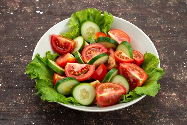 Vue avant de tomates en tranches avec des concombres à l'intérieur de la plaque blanche avec salade verte sur brown, déjeuner frais de légumes alimentaires sald