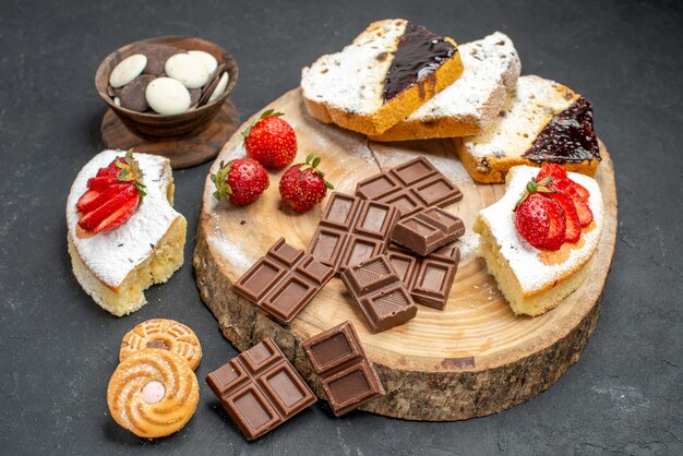 Vue avant des tranches de gâteau avec des barres de chocolat et des cookies sur fond gris