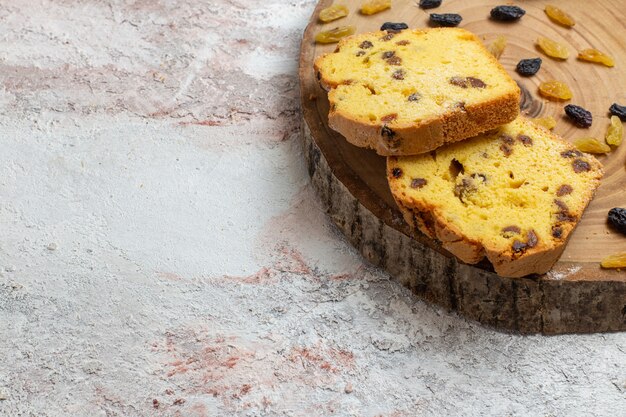 Vue avant des tranches de gâteau délicieux avec des raisins secs sur une surface blanche