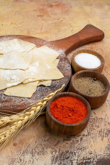 Vue avant des tranches de pâte crue avec des assaisonnements sur un plat de bureau en bois cuisine de pâtes