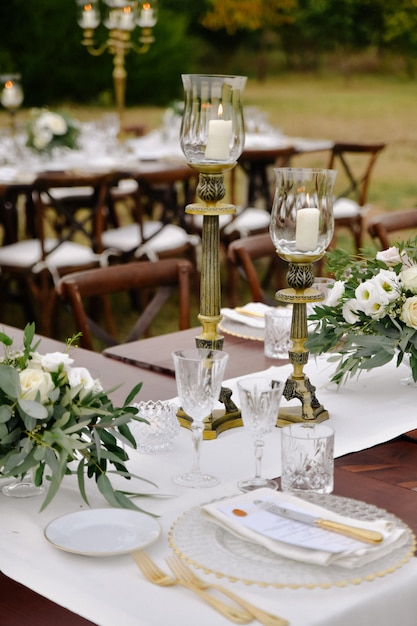 Photo gratuite vue avant de la verrerie et des couverts servis sur la table en bois avec des compositions florales et des chandeliers à l'extérieur