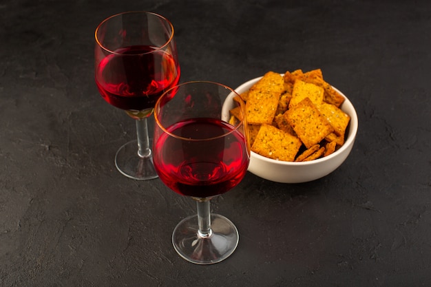 Une vue avant des verres de vin avec des chips à l'intérieur de la plaque sur dark