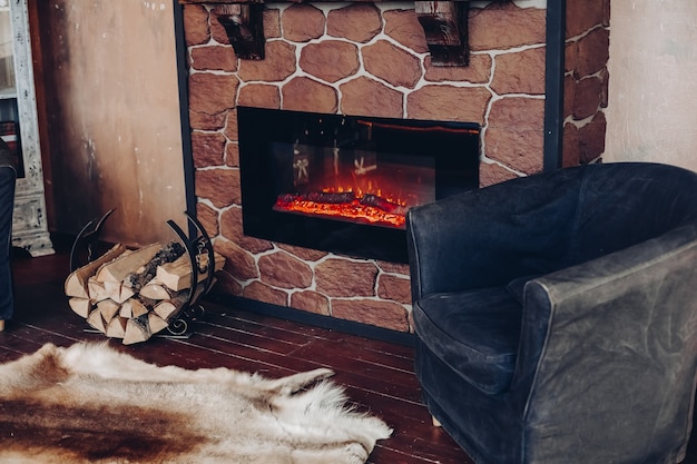 Vue sur cheminée avec bûches en feu, peau de fourrure naturelle sur le sol à côté du support avec bûches dans une pièce confortable.