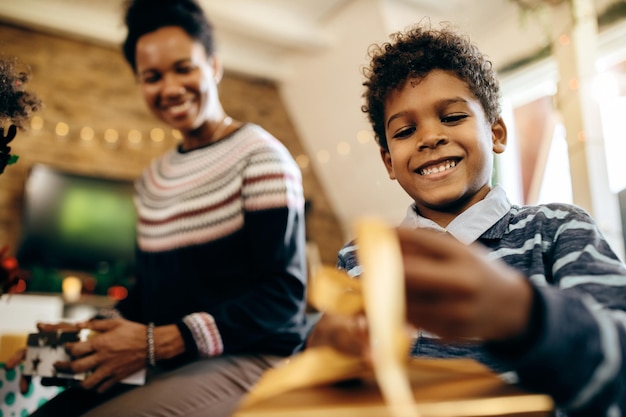 Vue ci-dessous d'un garçon noir heureux emballant des cadeaux de Noël avec sa mère à la maison