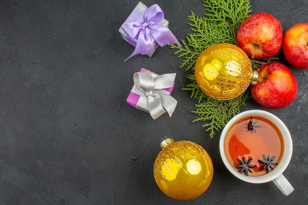 Vue ci-dessus des cadeaux et accessoires de décoration de pommes fraîches biologiques et une tasse de thé noir sur fond sombre