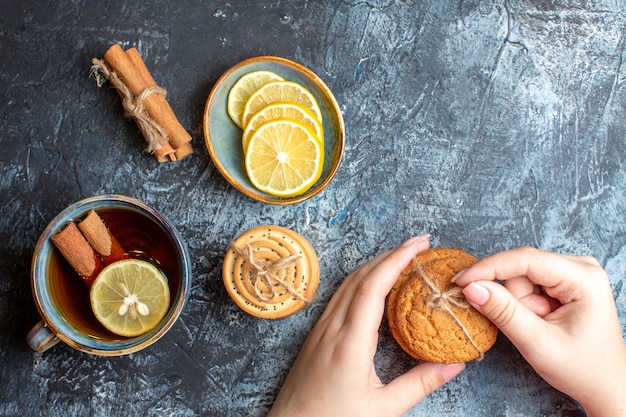 Vue ci-dessus de citrons frais et d'une tasse de thé noir à la main de cannelle tenant des biscuits empilés sur fond sombre