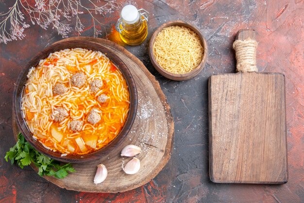 Vue ci-dessus d'une délicieuse soupe de nouilles avec du poulet sur une bouteille d'huile verte sur un plateau à l'ail sur une planche à découper sur fond sombre