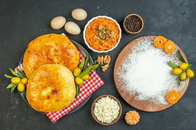 Vue ci-dessus de délicieuses pâtisseries fraîches et fromage poivrons oeufs farine mandarines sur la planche à découper en bois salade sur fond noir foncé