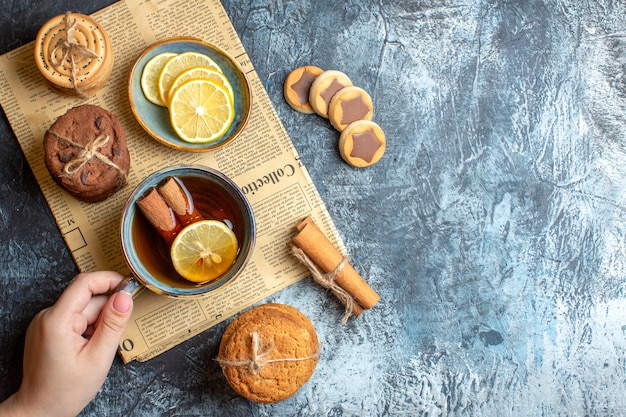 Vue ci-dessus de délicieux biscuits et main tenant une tasse de thé noir à la cannelle sur un vieux journal