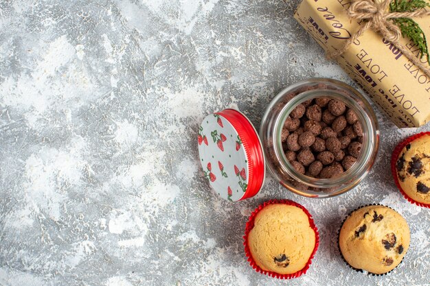 Vue ci-dessus de délicieux petits gâteaux et chocolat dans un pot en verre à côté du cadeau de Noël sur le côté gauche sur la surface de la glace