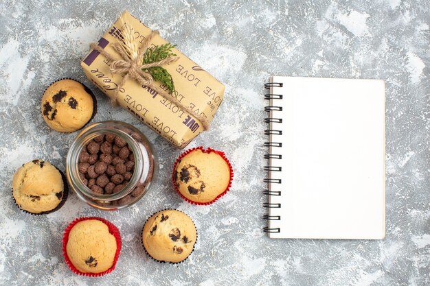 Vue ci-dessus de délicieux petits gâteaux et chocolat dans un pot en verre à côté du cadeau de Noël et du cahier fermé sur la surface de la glace