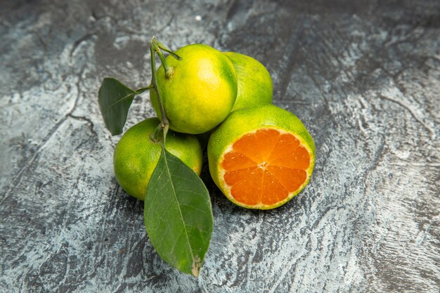 Vue ci-dessus de deux mandarines vertes entières avec des feuilles et une mandarine coupée en deux sur des images de fond gris