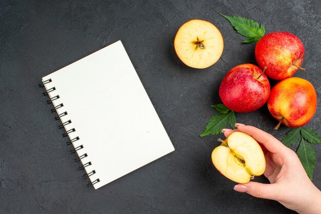 Vue ci-dessus du cahier et des pommes rouges fraîches coupées entières et des feuilles sur fond noir