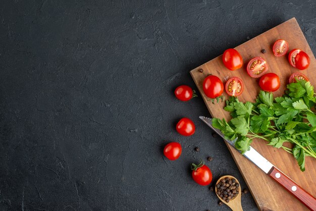 Vue ci-dessus du paquet vert de tomates entières fraîches coupées sur un couteau de planche à découper en bois sur le côté gauche sur une surface noire en détresse