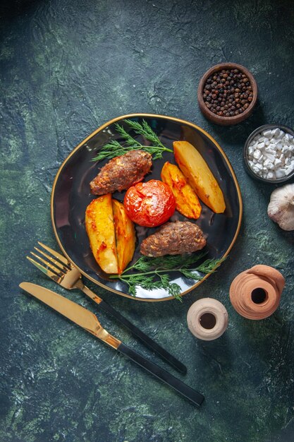 Vue ci-dessus des escalopes de viande cuites au four avec des pommes de terre et des tomates servies avec des couverts verts mis épices ail sur fond de couleurs mélangées