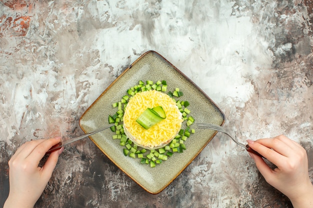 Photo gratuite vue ci-dessus d'une fourchette et d'un couteau sur une savoureuse salade servie avec du concombre haché sur un fond de couleur mélangée
