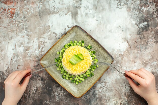 Vue ci-dessus d'une fourchette et d'un couteau sur une savoureuse salade servie avec du concombre haché sur un fond de couleur mélangée