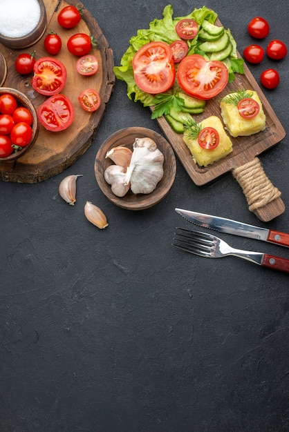 Vue ci-dessus de légumes frais et d'épices entiers coupés sur une planche en bois, une serviette blanche, des couverts, du fromage sur une surface noire