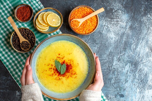 Vue ci-dessus de la main tenant une assiette bleue avec une soupe savoureuse servie avec de la menthe et du poivre sur une serviette verte dépouillé