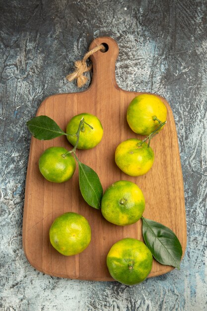 Vue ci-dessus des mandarines vertes avec des feuilles sur une planche à découper en bois sur fond gris