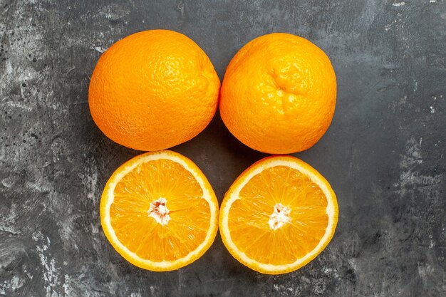 Vue ci-dessus d'oranges fraîches biologiques naturelles entières et coupées alignées en deux rangées sur fond sombre