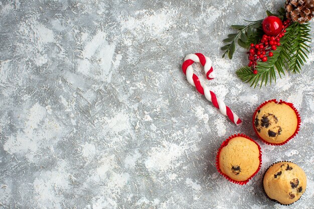 Vue ci-dessus de petits cupcakes bonbons et branches de sapin accessoires de décoration cône de conifère sur le côté droit sur la surface de la glace