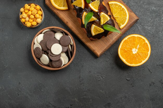 Vue ci-dessus de savoureux gâteaux oranges coupées avec des biscuits sur une planche à découper sur une table sombre