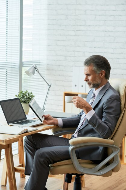 Vue côté, de, cadre supérieur, regarder, écran tactile tablette numérique, tout, en sirotant café