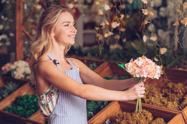 Vue de côté du joyeux sourire jeune femme fleuriste offrant l&#39;hortensia