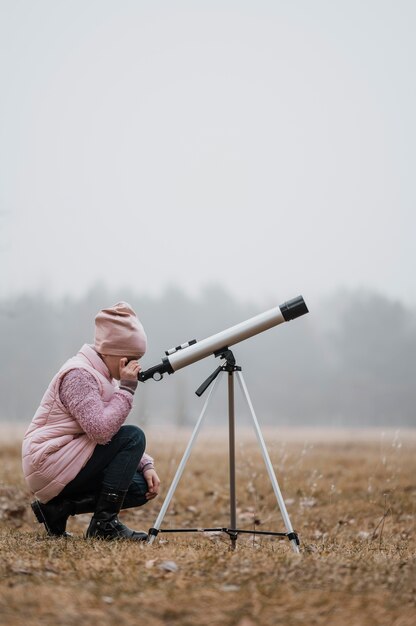 Vue de côté enfant à l'aide d'un télescope à l'extérieur