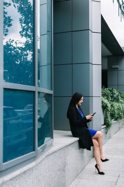 Photo gratuite vue de côté d'une femme d'affaires à l'aide de smartphone à l'extérieur de l'immeuble de bureaux