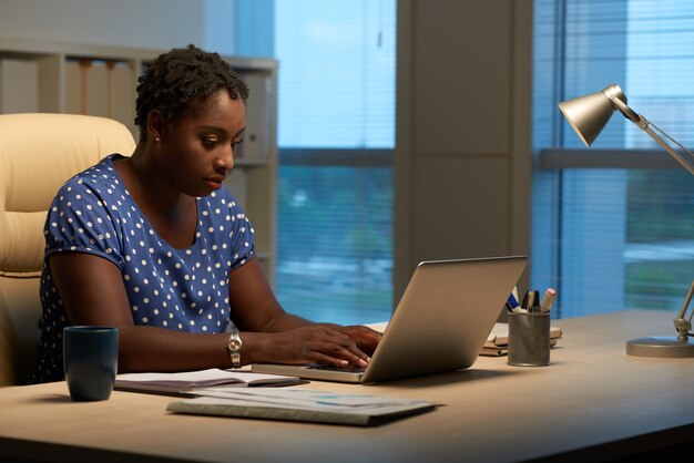 Vue de côté d'une femme cubaine répondant à des courriels au travail le soir