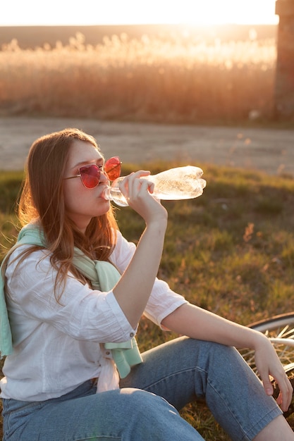 Photo gratuite vue côté, de, femme, eau potable, dans, les, coucher soleil